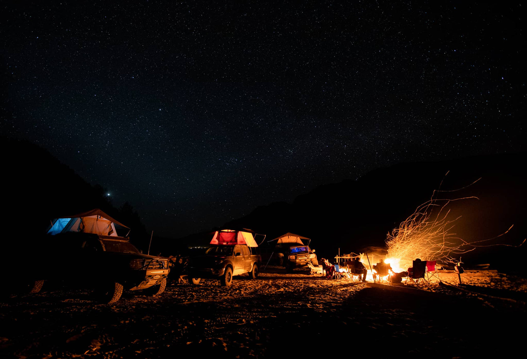 Camping scene at night with tents and a campfire under a starry sky.