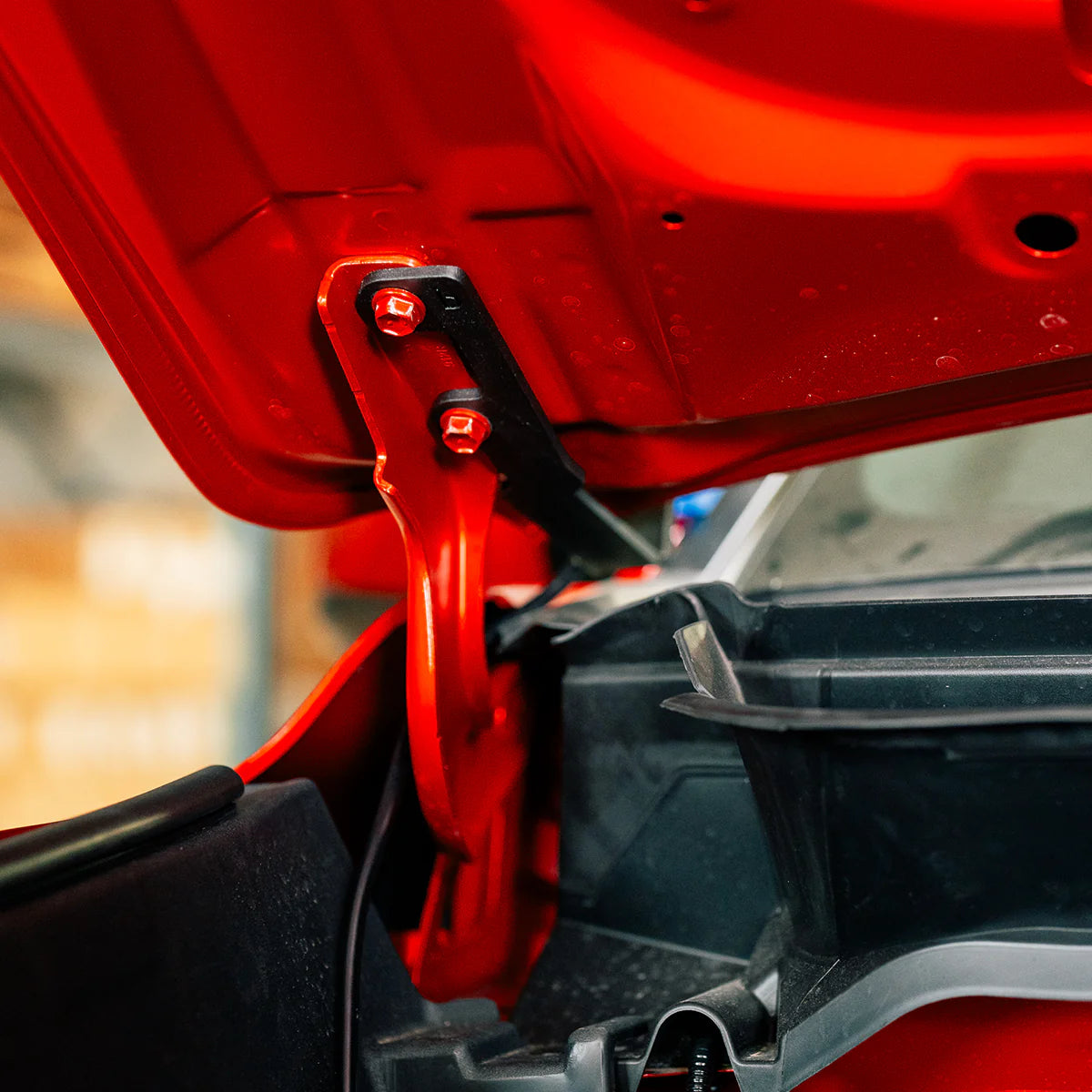 Close-up of a red car hood and light bracket with a blurred background