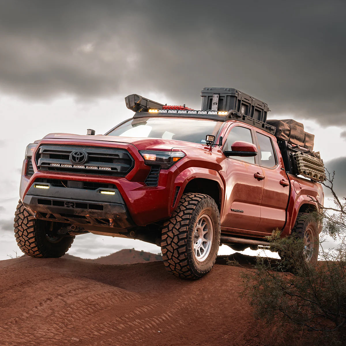 Red Toyota truck with off-road equipment on a rocky terrain under a cloudy sky