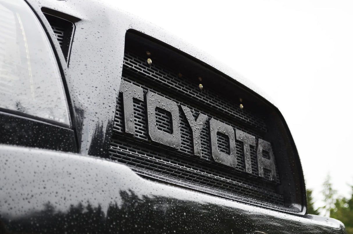 Close-up of a Toyota logo on a vehicle grille with raindrops.
