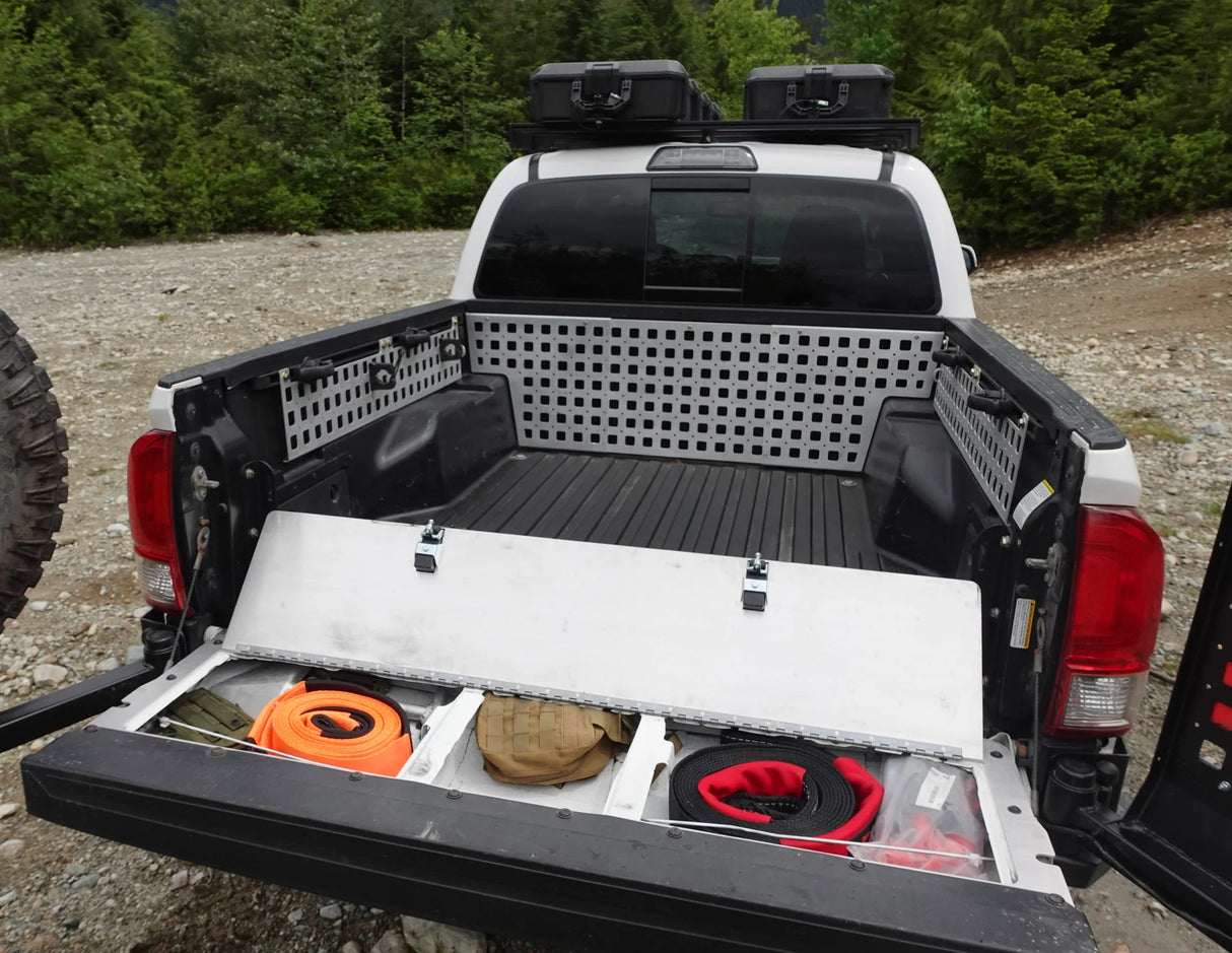 Truck bed with storage compartments and equipment, surrounded by trees.