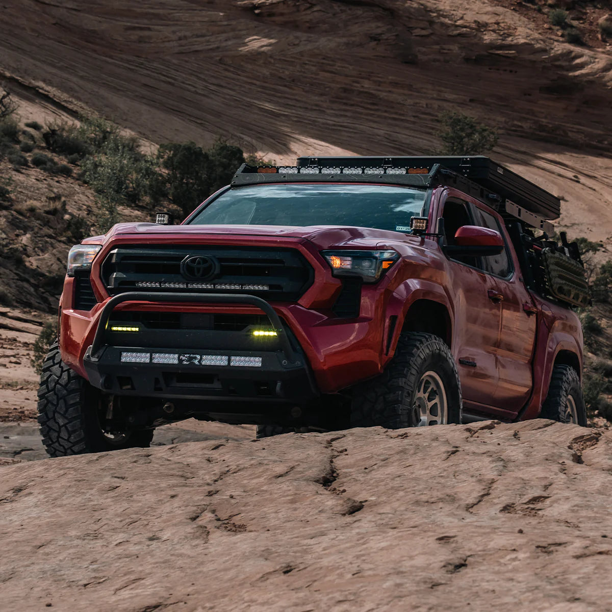 Red Tacoma climbing rocks with stealth bumper and bull bar