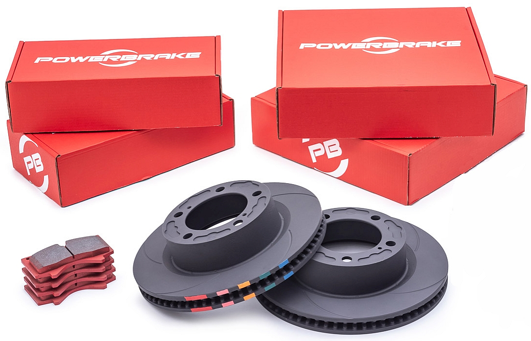 A set of PowerBrake D-Line front brake rotors and pads, including two rotors with slotted patterns and two sets of PB05 compound brake pads, alongside their red packaging boxes.