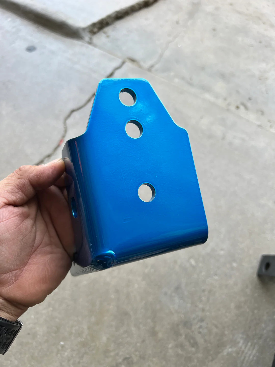 Blue metal bracket held by a hand on a concrete floor