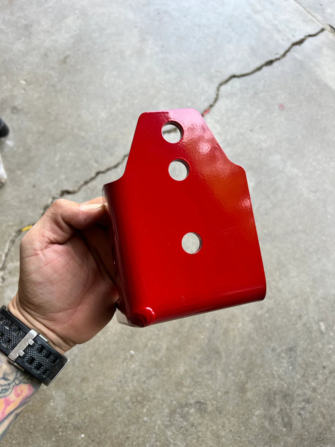 Red plastic block with holes held by a hand on a concrete floor
