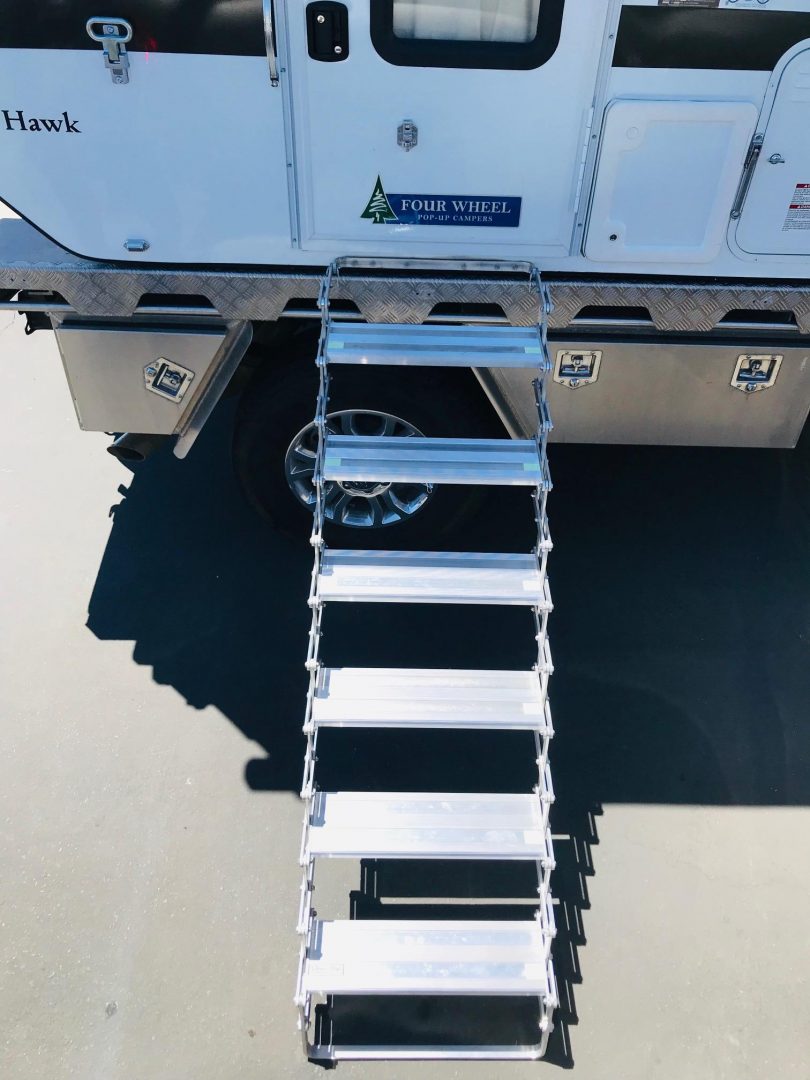Metal ladder extended from a vehicle with 'Four Wheel Campers' branding on a black surface.