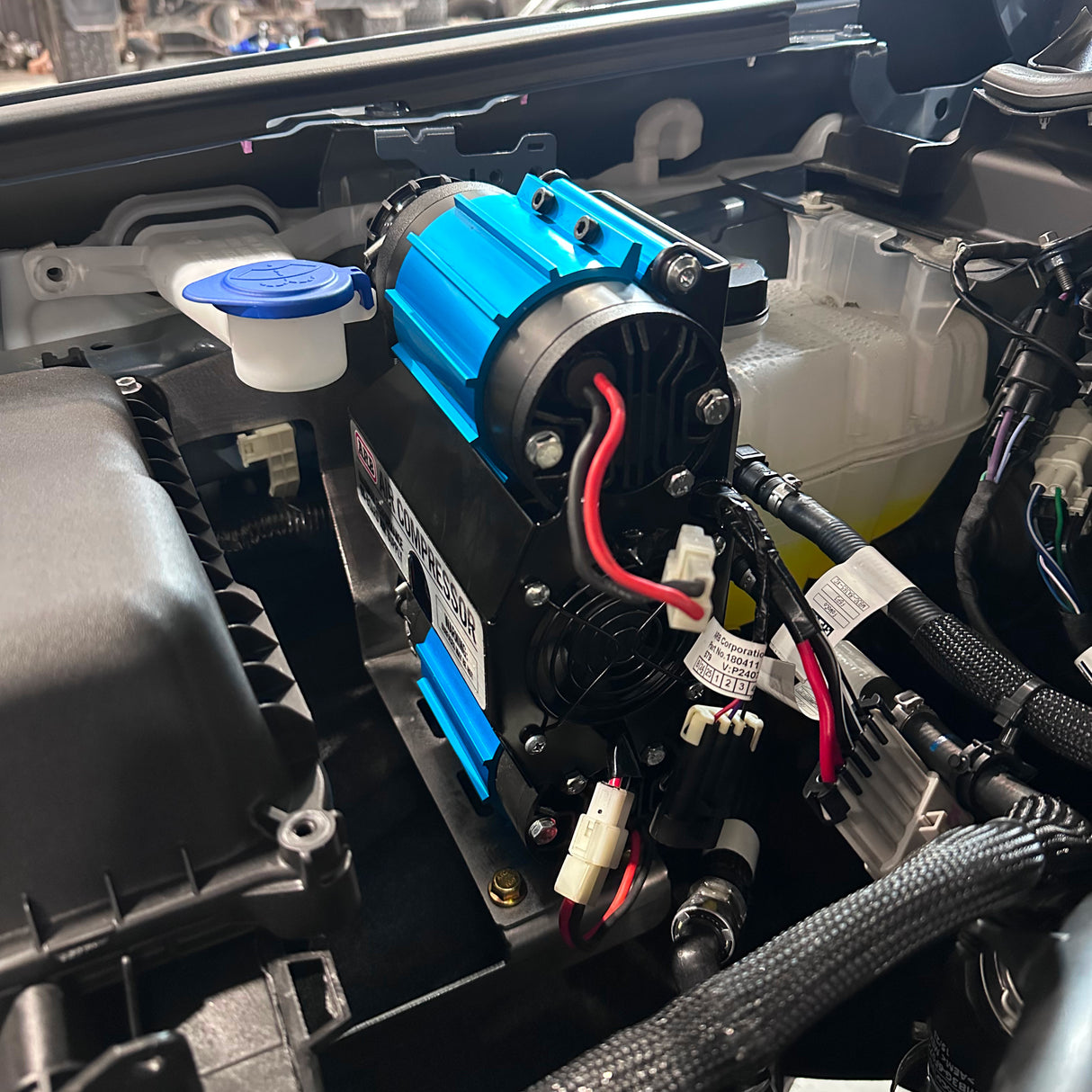 Close-up of a car's engine bay with a blue and black air compressor.