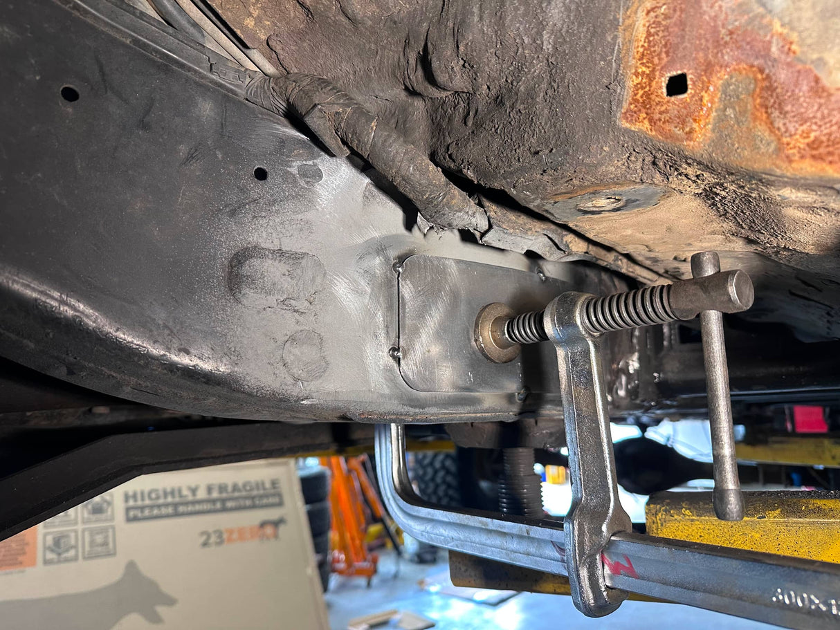 Close-up of a vehicle's undercarriage with a clamp on a workshop floor.