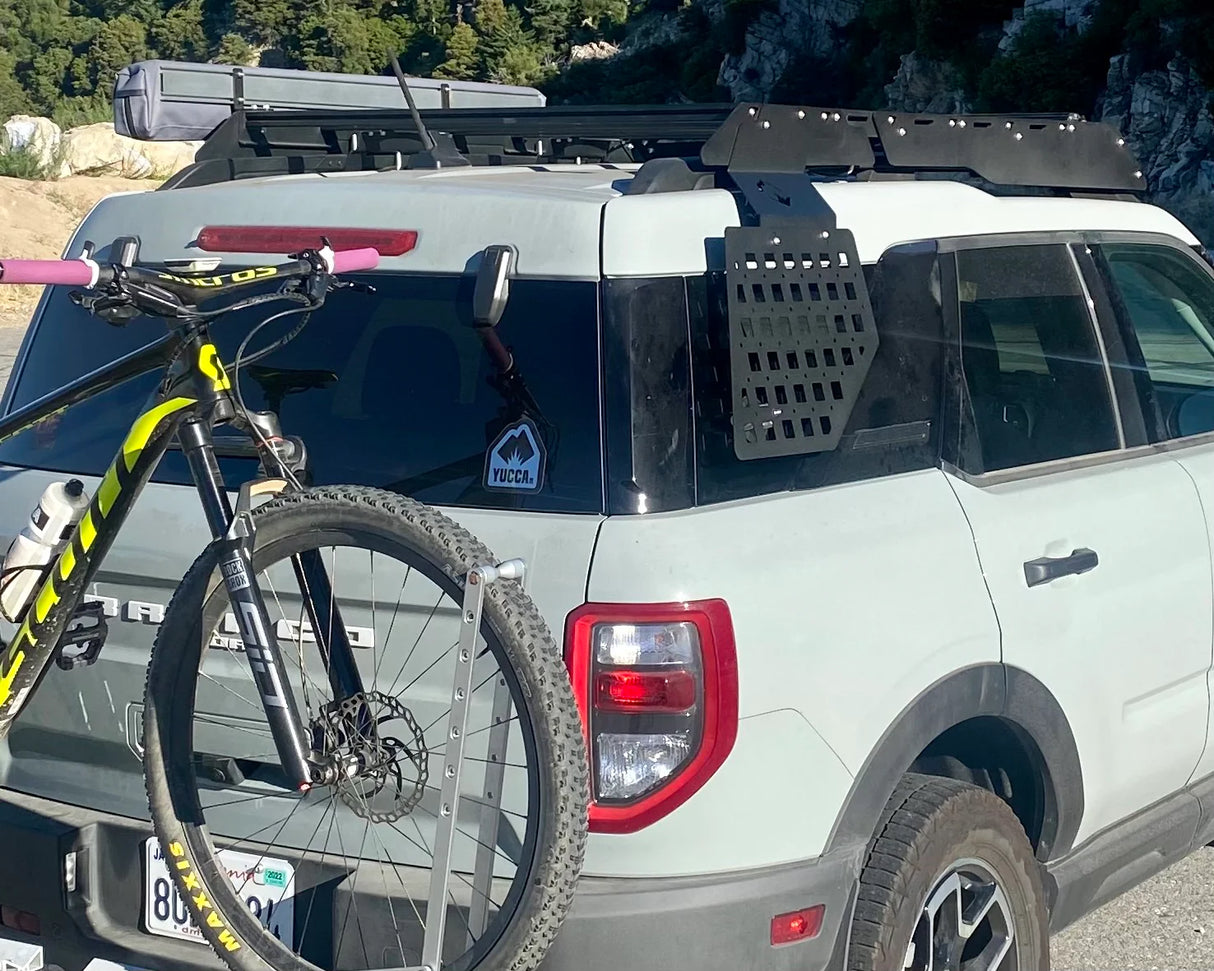 White SUV with a bike attached to its rear, parked outdoors with trees in the background