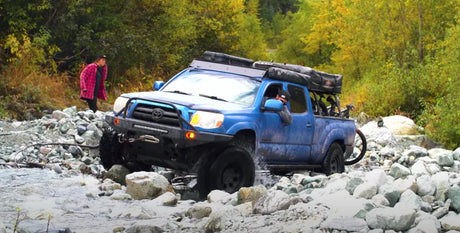 Blue Toyota truck with mods parks next to a river.