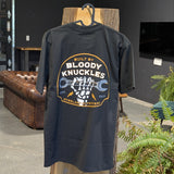 Back side of tee hanging on a wooden stand showing skeleton hand holding wrench