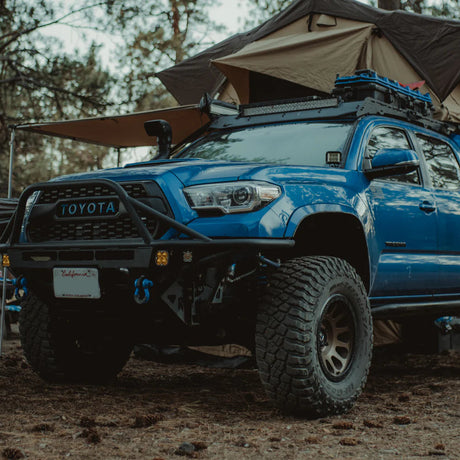 Blue Toyota truck with a rooftop tent in a forest setting