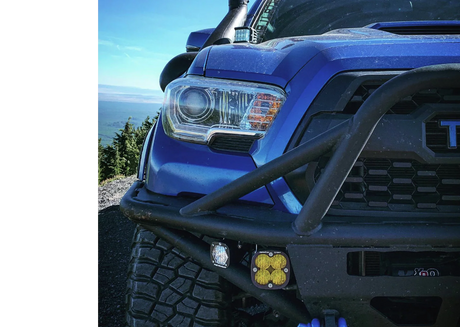 Close-up of a blue truck's front bumper with additional lights, set against a scenic background.