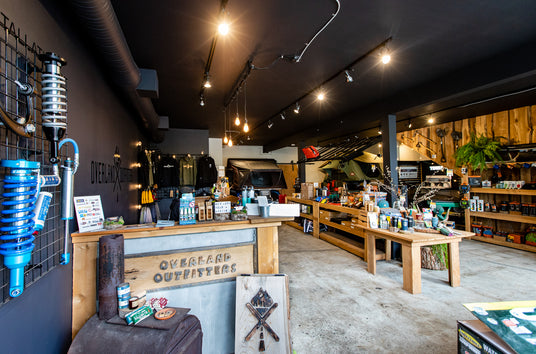 Overland Outfitters store showroom with shocks on the wall and assorted products on shelves and tables.