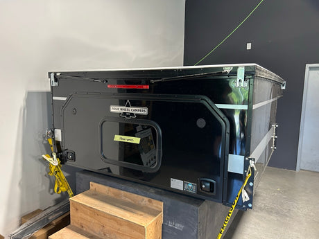 A black Fulek Wheel Ladders utility trailer or storage container with a small front window, photographed in an indoor warehouse or workshop setting.