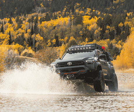 Toyota truck driving through water with a forest in the background