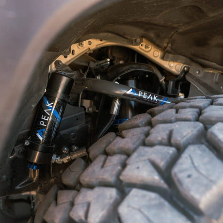Close-up of vehicle suspension system with 'Peak' branding on tire and undercarriage.