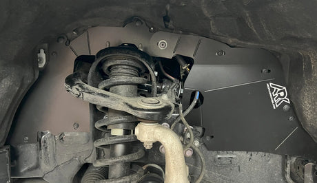 Close-up of a vehicle's undercarriage with suspension components and a black skid plate.