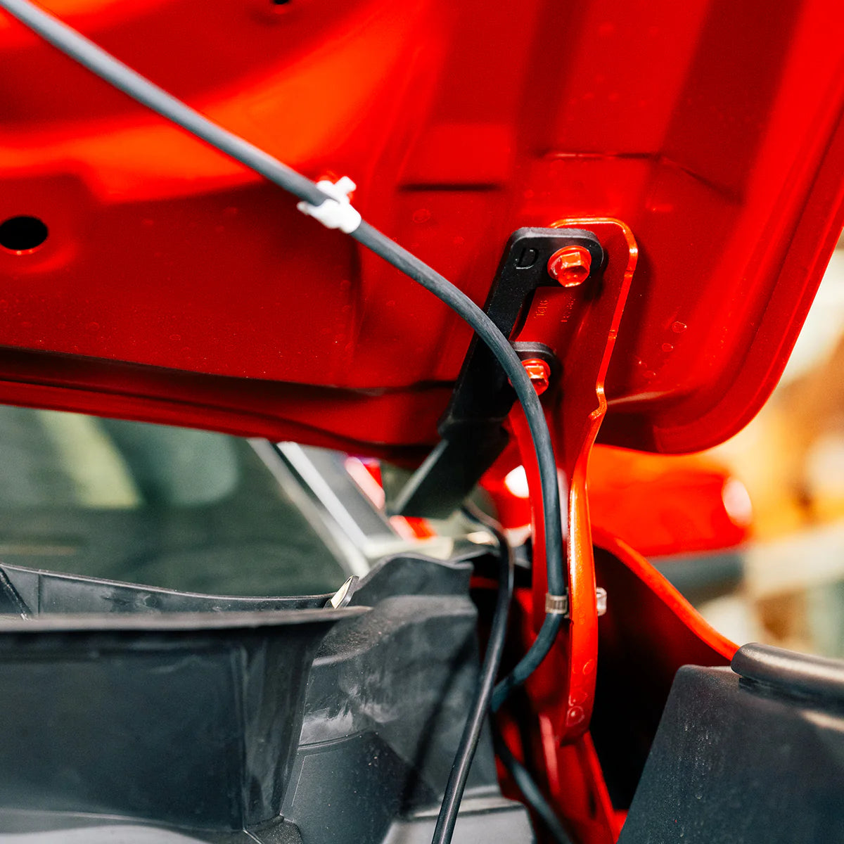 Close-up of a red car's open hood with visible wiring.