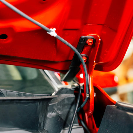 Close-up of a red car's open hood with visible wiring.
