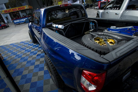 Blue truck with open bed showing mechanical components on a checkered floor.