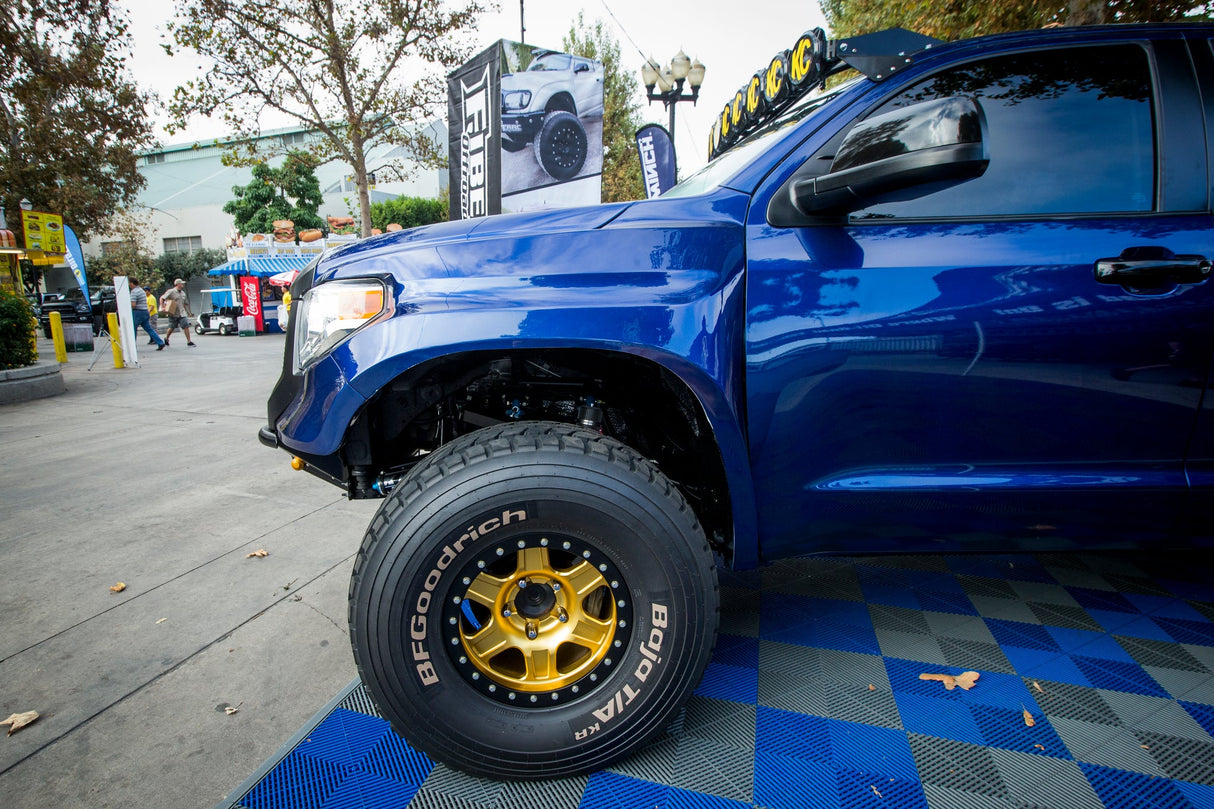 Blue truck with large off-road tires on a checkered floor