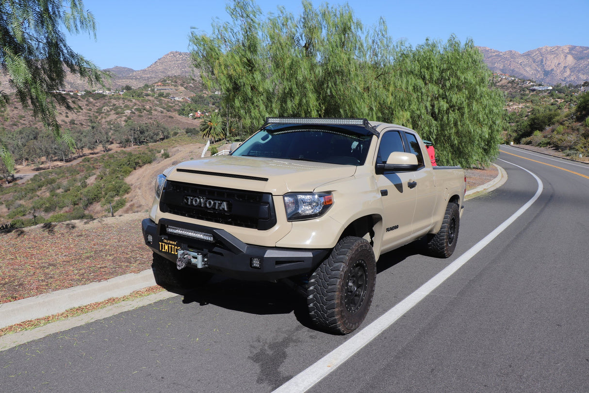 Beige Toyota truck on a road with greenery and mountains in the background
