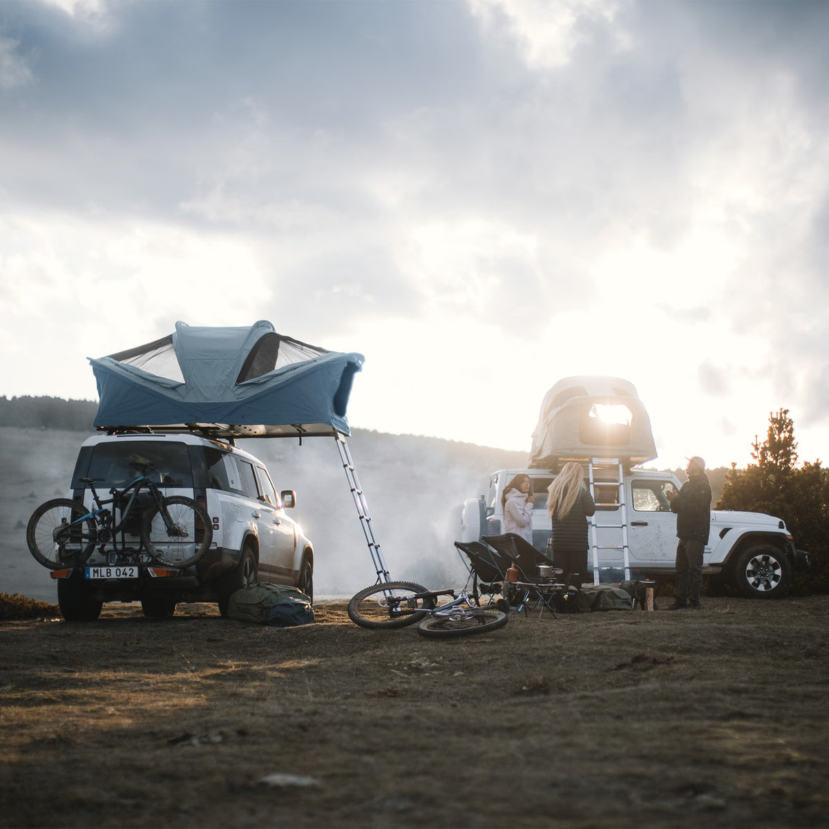 Two vehicles with rooftop tents in a natural setting with people around.