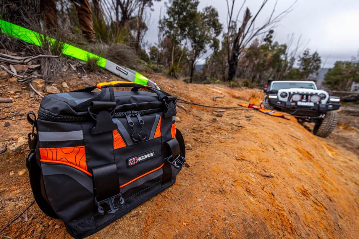 recovery kit bag on terrain in foreground with an off road vehicle being towed in the background