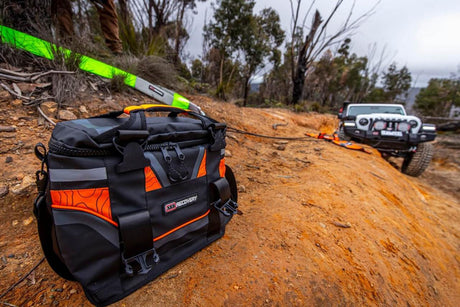 recovery kit bag on terrain in foreground with an off road vehicle being towed in the background