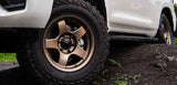 Close-up of a vehicle tire with a bronze alloy wheel on a dirt road.