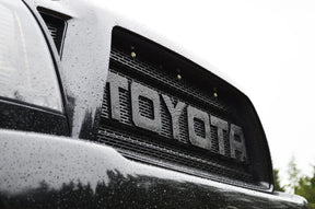 Close-up of a Toyota logo on a vehicle grille with raindrops.