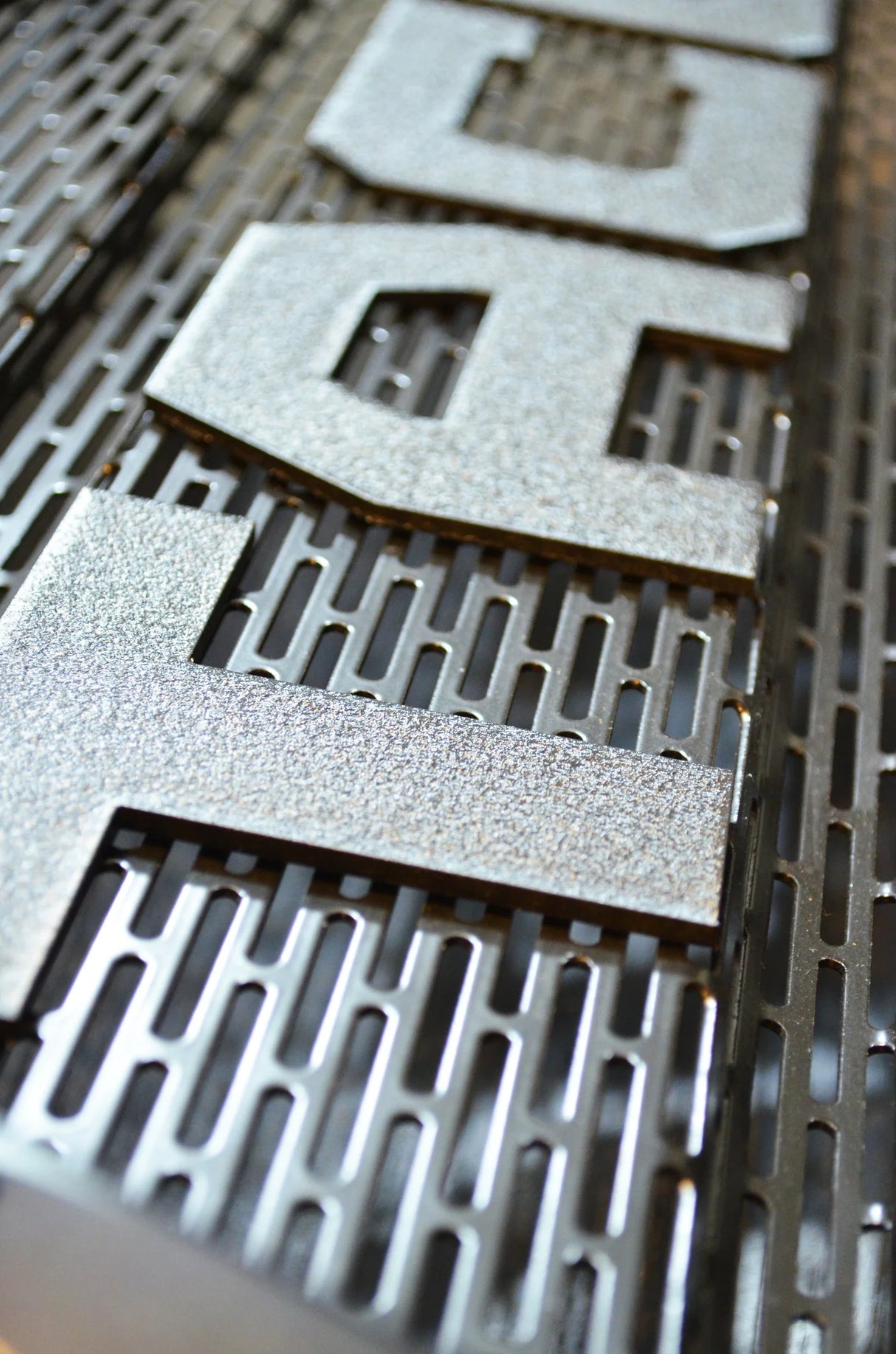 Metallic letters spelling 'DEG' on a textured metal surface