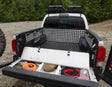 Truck bed with storage compartments and equipment, surrounded by trees.