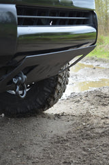 Close-up of a vehicle's front bumper and tire on a muddy road