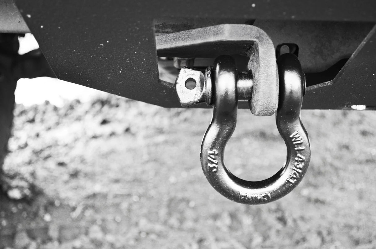 Metal shackle attached to a vehicle's hitch receiver on a gravel surface