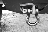 Metal shackle attached to a vehicle's hitch receiver on a gravel surface