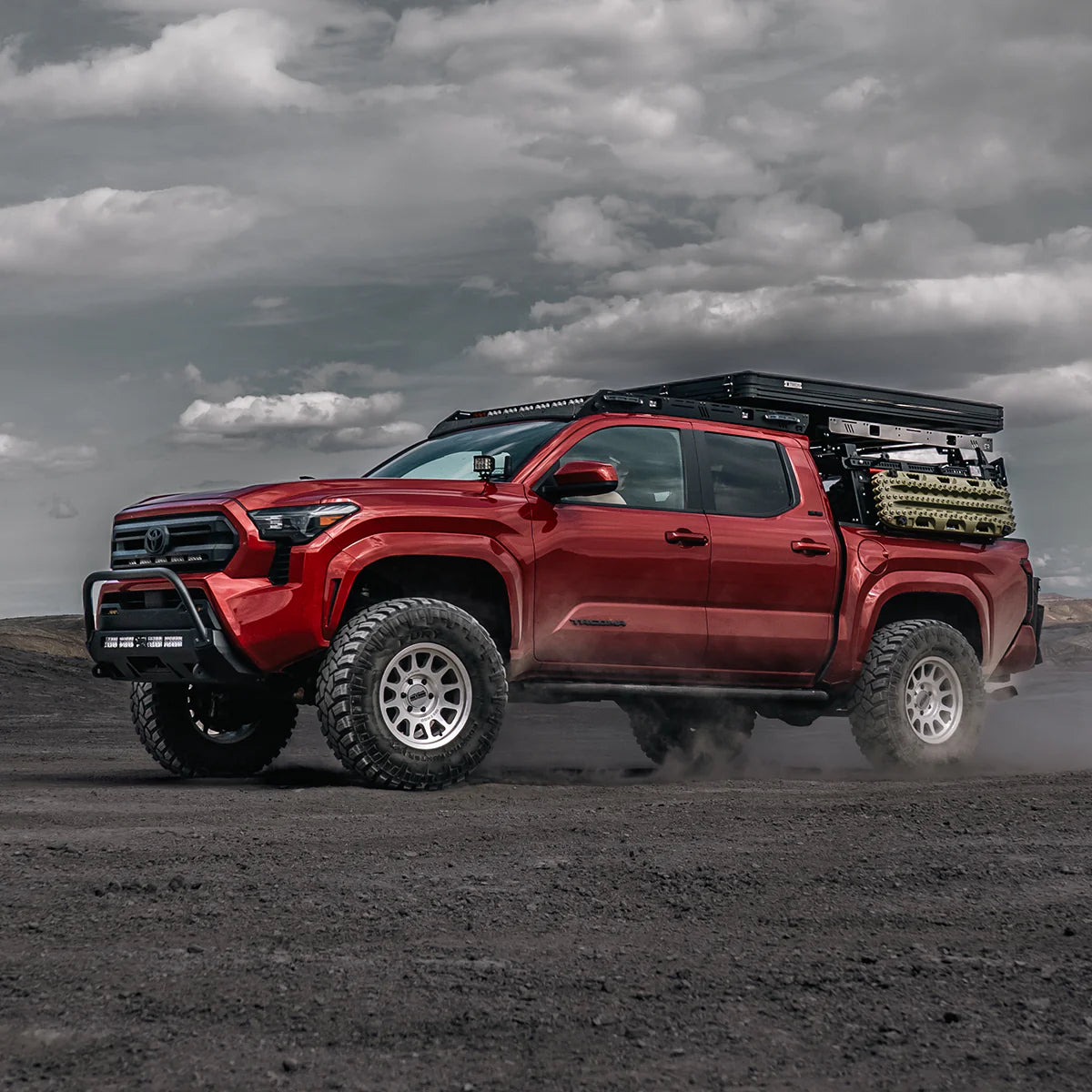 Red Tacoma truck with stealth bumper on a dirt road under a cloudy sky