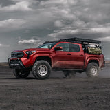 Red Tacoma truck with stealth bumper on a dirt road under a cloudy sky