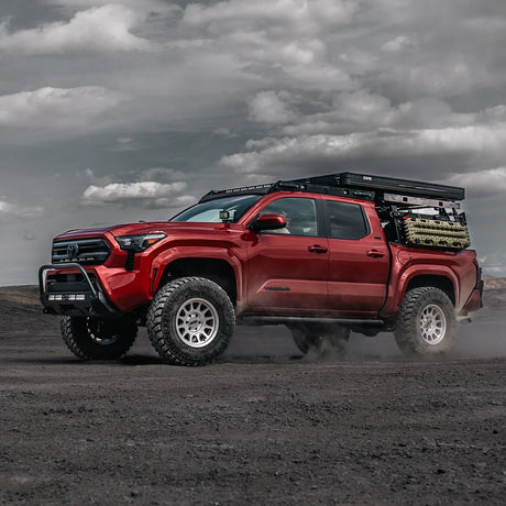 Red Tacoma truck with stealth bumper on a dirt road under a cloudy sky