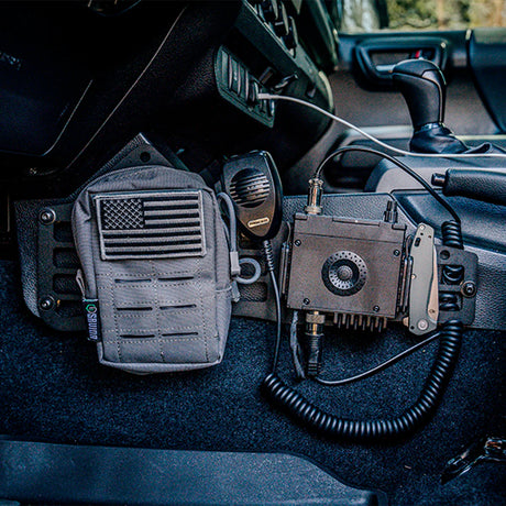 Tactical radio and equipment on a vehicle dashboard with American flag patch.
