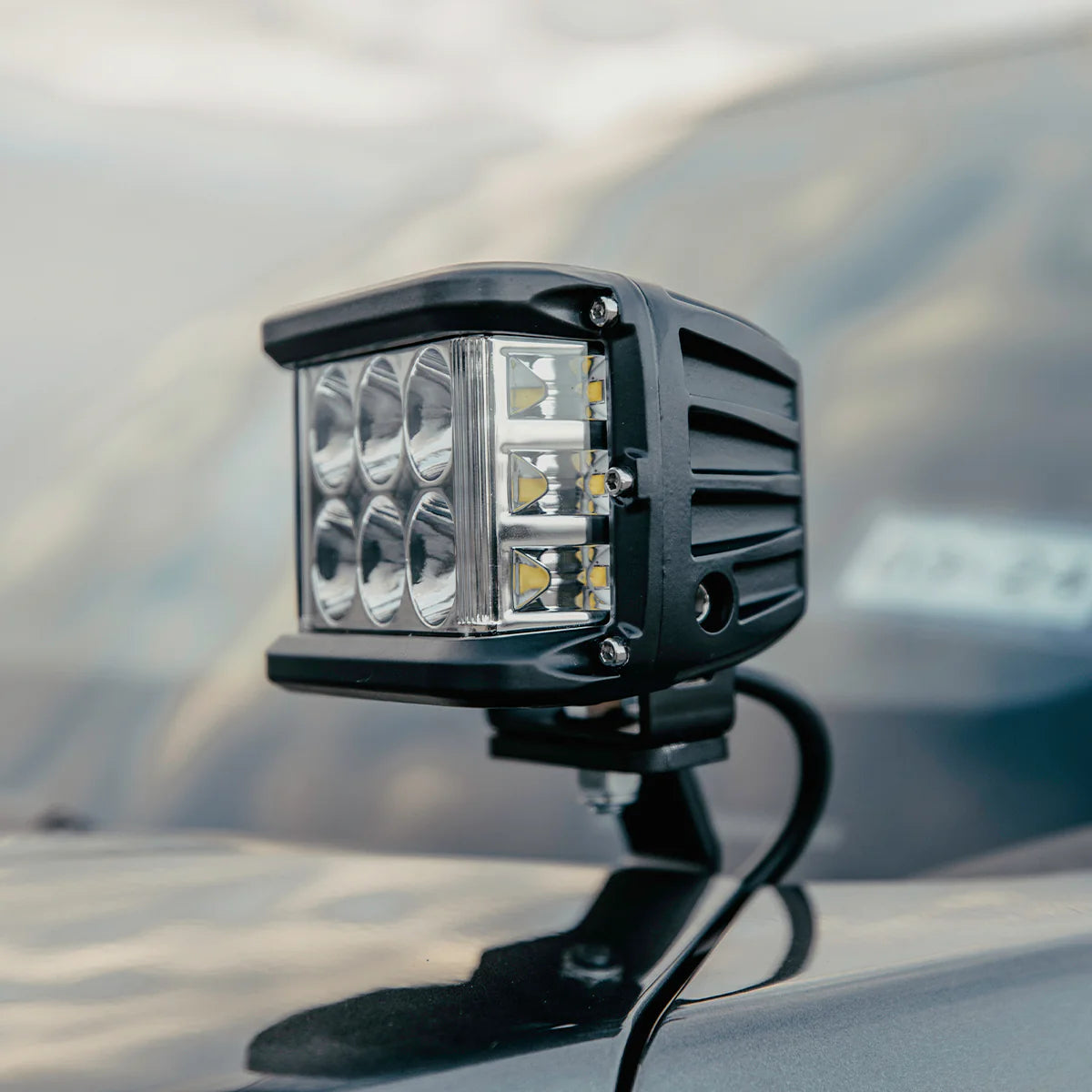 Cube-shaped LED work light on a vehicle's roof with a blurred background