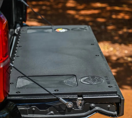 A black plastic tailgate insert for a Toyota Tacoma, displayed in an installed position on the truck's bed.