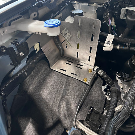 Close-up of a car's engine compartment with a metal bracket and fluid reservoir.