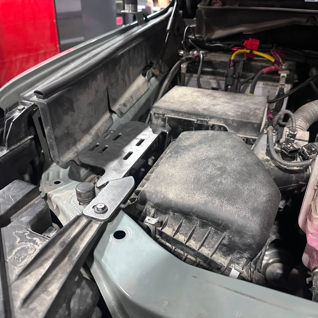 Car engine compartment with visible components and wiring.