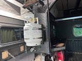 Propane tank secured in a bracket mounted to the back of a truck bed camper.