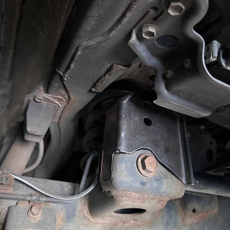 Close-up of mechanical components under a vehicle, showing rust and wear.