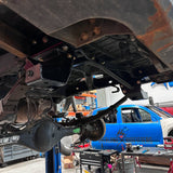 Close-up of a vehicle's undercarriage with a blue truck in the background.