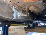 Close-up of a car's undercarriage with visible rust and mechanical components.