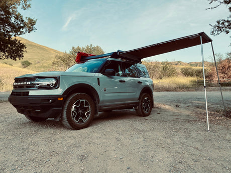 Ford Bronco with a roof rack and extended canopy in a natural setting
